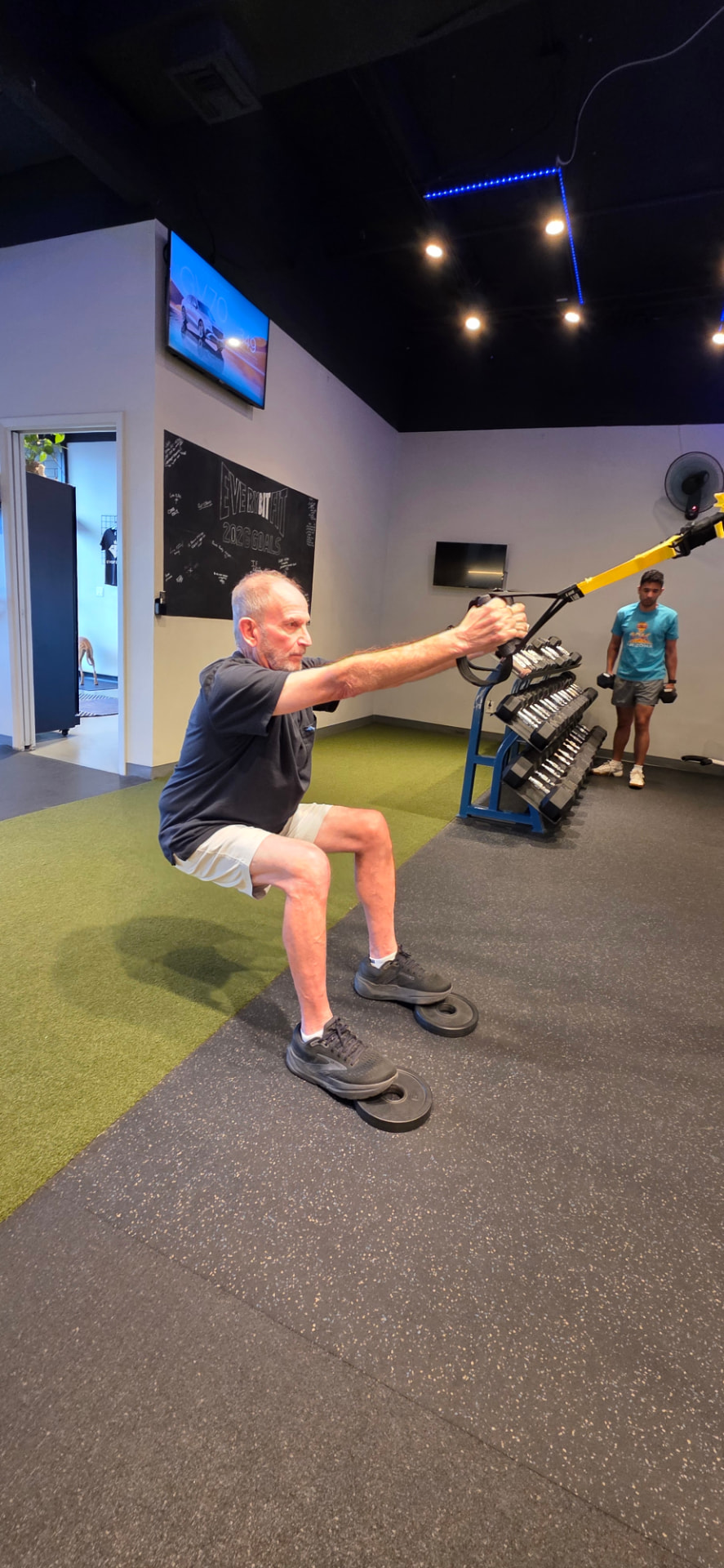 Older adult performing assisted squats with a trainer spotting at Everybitfit
